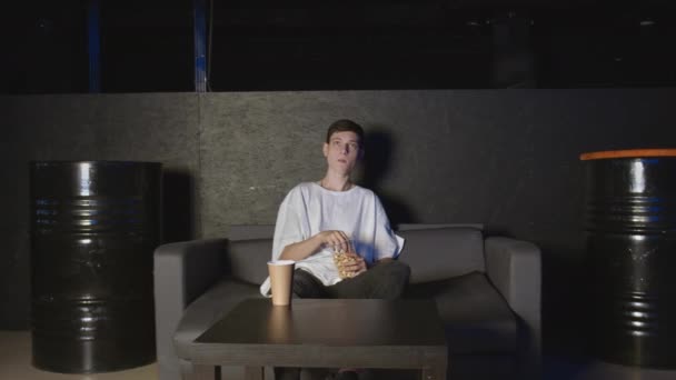 Junger Mann isst Popcorn und schaut zu Hause vor dem Fernseher entspannt auf der Couch — Stockvideo