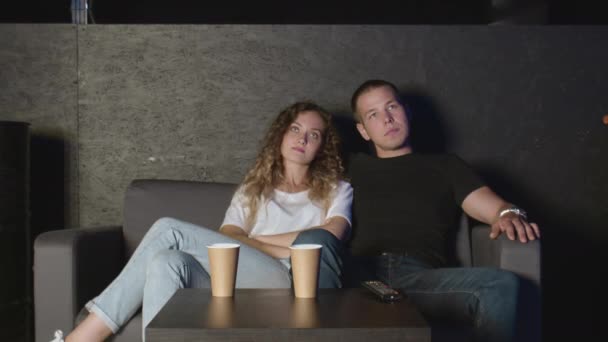 Mladý pár milénií sedí na gauči před televizí — Stock video