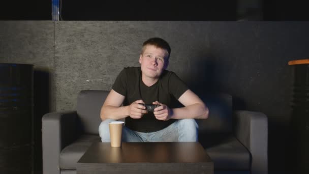 Junger Mann spielt Konsolenspiel vor der Kamera und schlägt seinen Gegner online. Weißer Mann auf dem Sofa. — Stockvideo