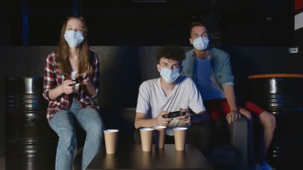 Three friends with face masks in front of the screen are playing together in the online battle — Stock Video