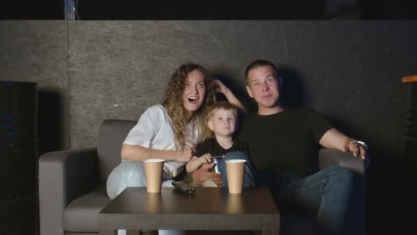 Счастливые родители и маленький сын смеются, смотря телевизор вместе — стоковое видео