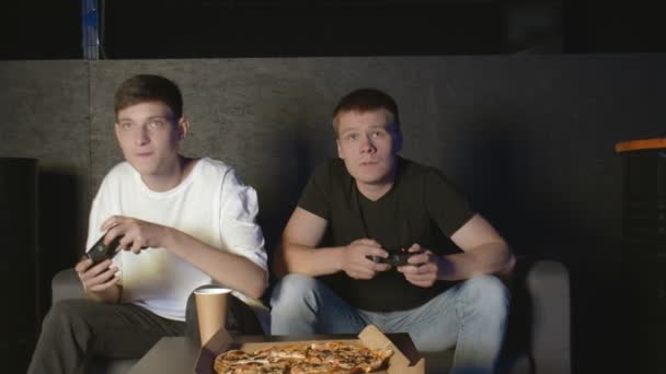 Dans le salon Deux amis assis sur un canapé Jouer au jeu vidéo et manger de la pizza. — Video