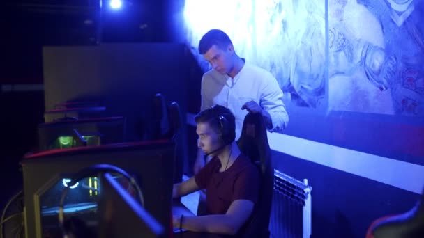 Νεαρός άνδρας βοηθά το φίλο του να κερδίσει γύρο στο shooter video game στο σύγχρονο cybersport club — Αρχείο Βίντεο