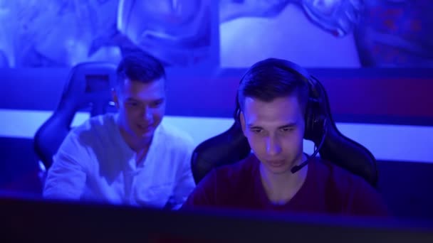 Молодой человек дает советы своему другу, пока он играет в видеоигры в современном киберспортивном клубе — стоковое видео