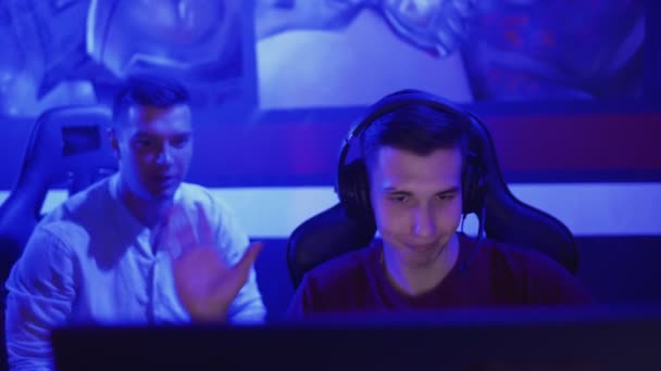 Jeune homme donnant des conseils à son ami pendant qu'il joue au jeu vidéo dans le club cybersport moderne — Video