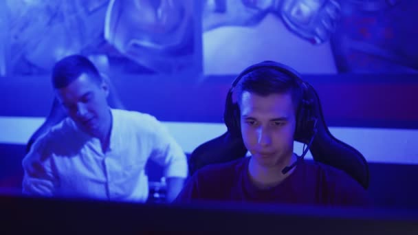 Jongeman geeft advies aan zijn vriend terwijl hij speelt ronde van video game in moderne cybersport club — Stockvideo
