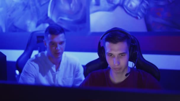 Jeune homme donnant des conseils à son ami pendant qu'il joue au jeu vidéo dans le club cybersport moderne — Video