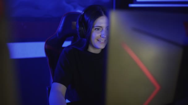 Gyönyörű fiatal nő ül a fejhallgató és játszik egy online játék egy számítógépes klubban. A nő lelkesen játszik és beszél a partnereivel a mikrofonon. Portré nézet. — Stock videók