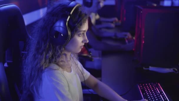 Mujer joven se sienta en el club de informática y juega un juego en línea. Club de ordenador moderno. — Vídeo de stock