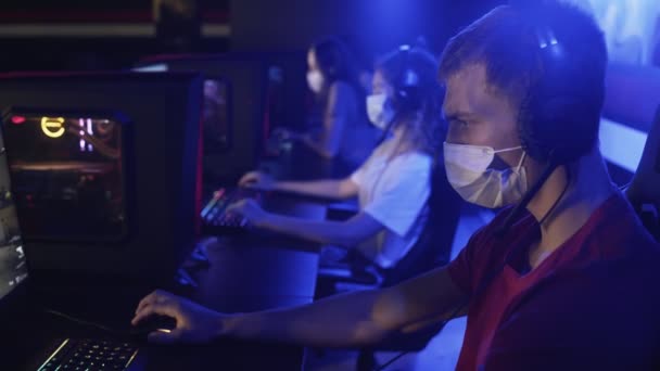 Primer plano de los jugadores jóvenes en máscaras faciales juega en los videojuegos en el club de computadoras moderno. — Vídeo de stock