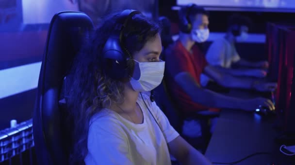 Vista lateral de la joven jugadora en máscaras faciales juega en los videojuegos en el club de computadoras moderno. — Vídeo de stock