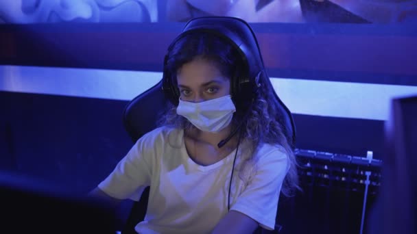 Mujer aburrida en máscaras faciales juega en los videojuegos en el club de computadoras moderno. — Vídeo de stock