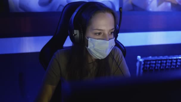 Mujer concentrada en máscaras faciales juega en los videojuegos en el club de computadoras moderno. — Vídeos de Stock