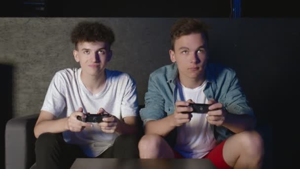 Dois caras chateados estão sentados no sofá na frente da TV e perdendo em um jogo no console — Vídeo de Stock