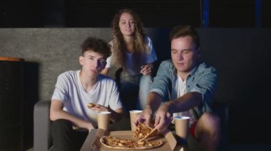 Genç arkadaşlar oyun konsolunu bitirdiler ve karanlık odada pizza yemeye başladılar..