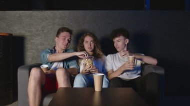 Oturma odasında TV seyreden en iyi üç arkadaş ve patlamış mısır yiyor.