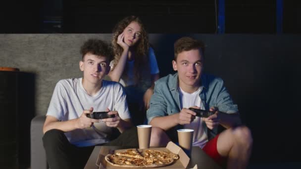 Os amigos jogam no console do jogo. Eles estão sentados no sofá e segurando os joysticks. Um homem a ganhar outro a perder — Vídeo de Stock