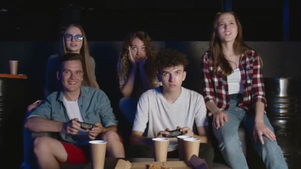 Grupo de amigos se divierten con el videojuego en casa, un chico está ganando riendo y haciendo chocar los cinco, otro chico está molesto. — Vídeos de Stock