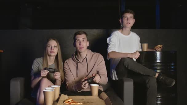 Skupina koncentrovaných přátel hraje ve hře konzole, žena proti muži. Jí pizzu — Stock video