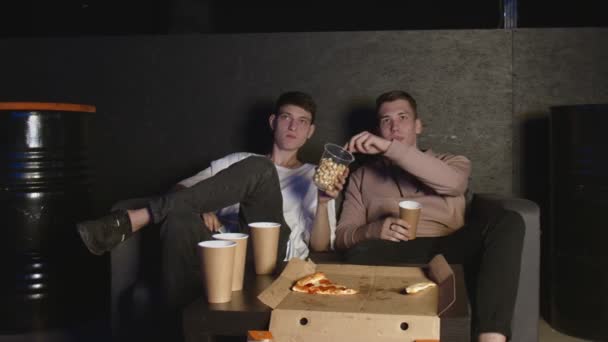 В гостиной двое лучших друзей смотрят телевизор и едят попкорн — стоковое видео