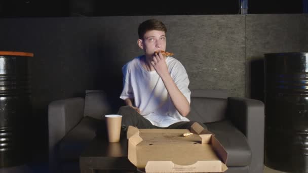 Jongeman die pizza eet en thuis tv kijkt ontspannen op de bank — Stockvideo