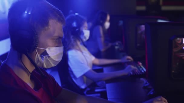 Закриття молодих геймерів в масках для обличчя грає в відеоіграх в сучасному комп'ютерному клубі. — стокове відео
