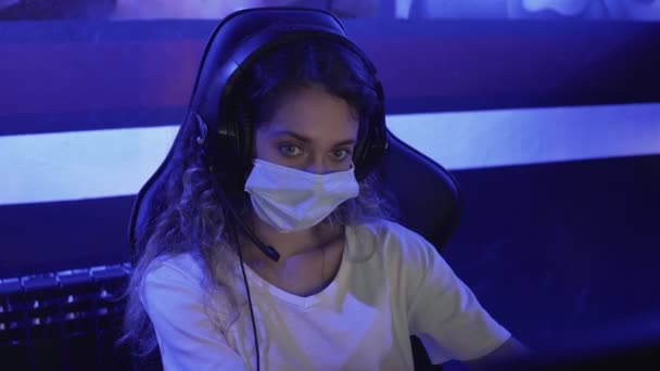 Mujer aburrida en máscaras faciales juega en los videojuegos en el club de computadoras moderno. — Vídeos de Stock