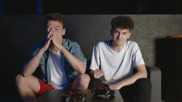 Two ANGRY guys are sitting on the couch in front of the TV and losing in a game on console — Stock Photo, Image