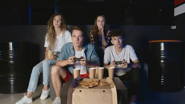 Jóvenes amigos jugando en la consola de juegos. Dos hombres sostiene controladores y juega mientras novias relojes — Foto de Stock