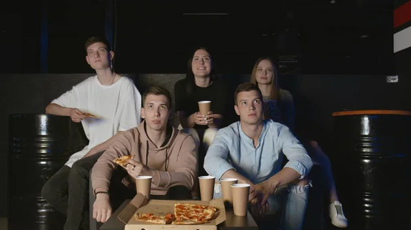 Group of young friends watching television together on couch, communicating, eating popcorn and pizza — Stock Photo, Image