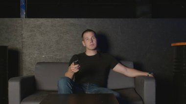 Adam kanepede oturur ve televizyon izler..