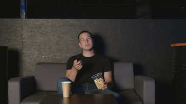 Yakışıklı adam patlamış mısır yiyor ve evde televizyon seyrediyor. Uzaktan kumandayla kanepede dinleniyor.