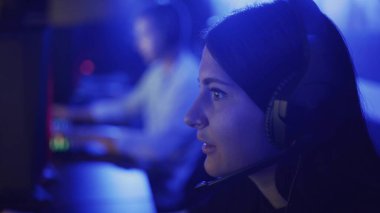 Güzel bir kadın modern bir bilgisayar kulübünde online oyun oynuyor. Genç kadın kulaklıkla monitörün önünde oturuyor, dikkatli bakıyor ve gülüyor. Bilgisayar oyununda sevinç ve şaşkınlık hissi