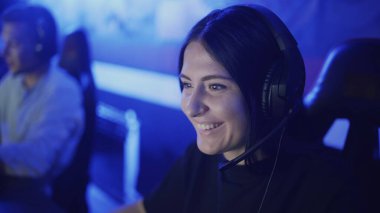 Modern bir bilgisayar kulübünde kulaklık takan mutlu bir kadın online oyun oynuyor..