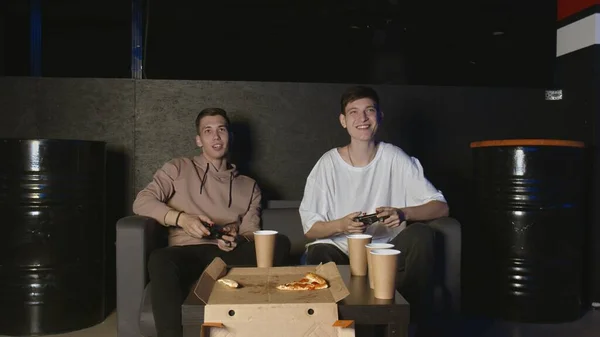 Two handsome young guys playing video games eating pizza