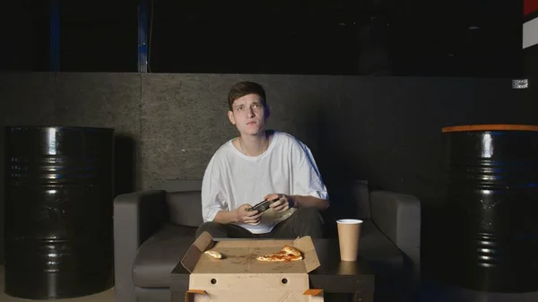 Jeune homme attrayant jouant à des jeux vidéo en utilisant la console de jeu étant nerveux assis sur le canapé à l'intérieur dans l'appartement — Photo