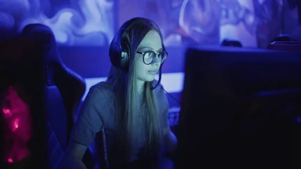 Jovem concentrada com óculos e fones de ouvido se senta na frente do monitor e joga em videogame no clube de informática — Fotografia de Stock
