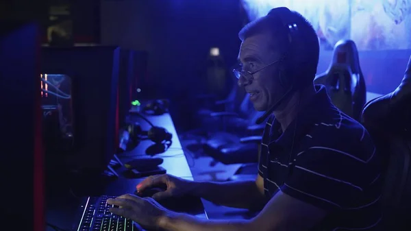 Старий грає на комп'ютері пізно вночі в сучасному комп'ютерному клубі . — стокове фото