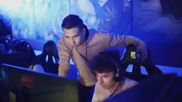 Тренер Pro Gamers дає поради своєму другу, поки він грає в раунд відеоігор в сучасному кіберспортивному клубі — стокове фото