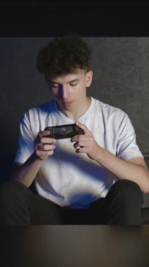 Evdeki kanepede video oyunu oynayan genç bir adamın ön görüntüsü VERTICAL VIDEO