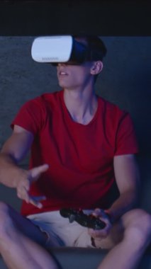 Akşamları çağdaş odadaki koltukta oturan sanal gerçeklik kulaklıklı çekici genç adam VERTICAL Video