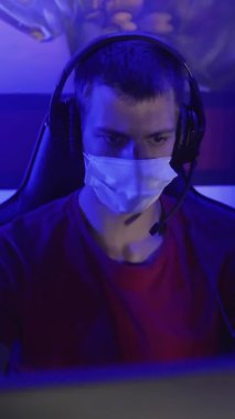 Modern bilgisayar kulübünde maskeli genç oyuncular oyun oynuyorlar. VERTICAL VIDEO