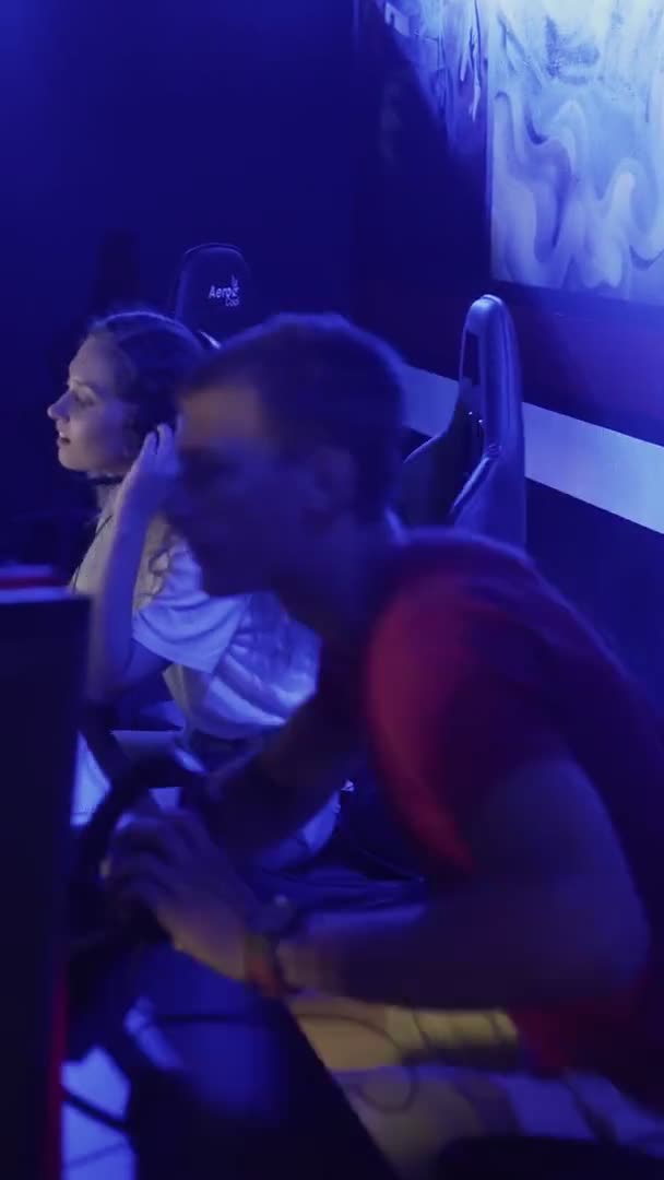 Joyeux jeune homme aidant sa petite amie à gagner tour dans le jeu vidéo de tir dans le club cybersport moderne VERTICAL VIDEO — Video