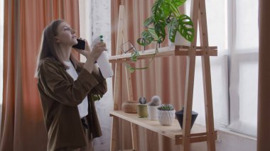 Kadın çiçekçi telefonda konuşuyor ve çiçekleri suluyor.