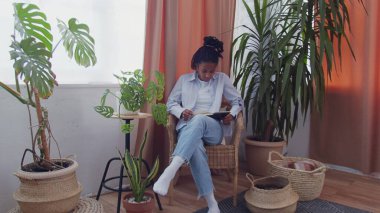 Güzel Afro-Amerikalı kadın hasır koltukta oturup kitap okuyor.