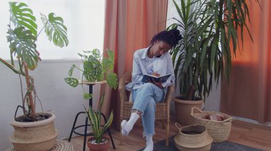 Çekici meşgul Afrikalı genç bir kadın çiçeklerle çevrili oturur, telefonda konuşur ve not defterine bazı notlar alır.