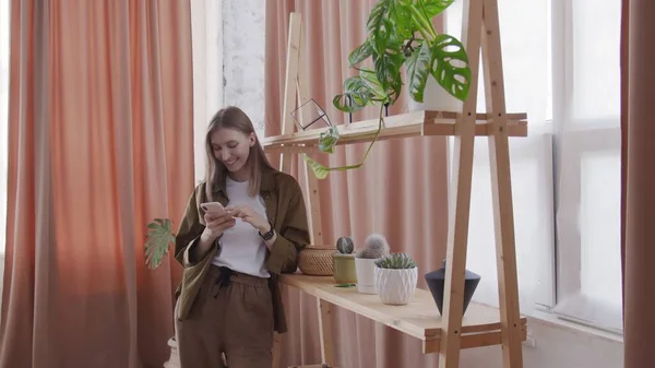 Attractive woman uses phone near the shelf with flowers — Stock Photo, Image