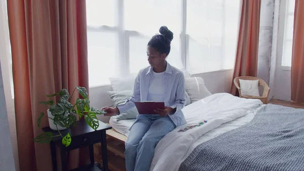 Junge Afroamerikanerin sitzt im Bett und malt Bild ihrer Hausblume — Stockfoto