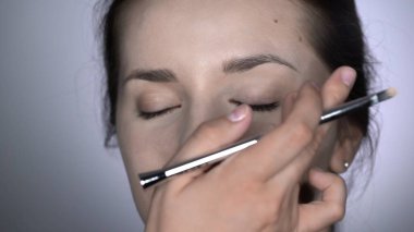Stüdyoda oturan güzel ve muhteşem kadın için profesyonel makyaj süreci. Makyaj Sanatçısı göz kapağına kapatıcı uygular