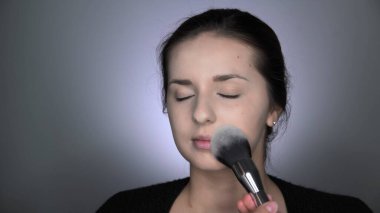 Stüdyoda oturan güzel ve muhteşem kadın için profesyonel makyaj süreci. Makyaj sanatçısı tozu büyük bir fırçayla uygular